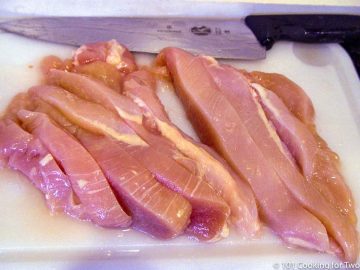 chicken cut into strips on a white board
