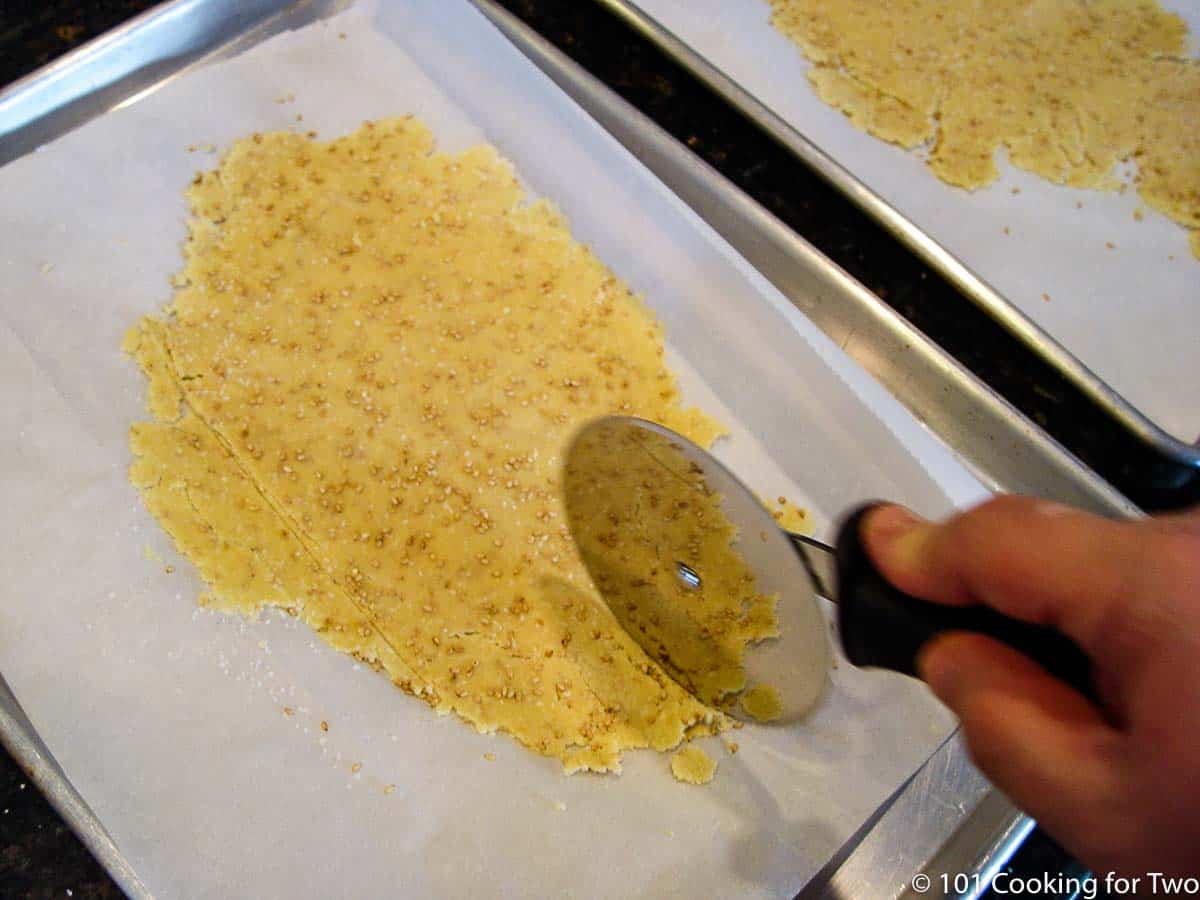 cutting raw cracker dough with a pizza cutter.