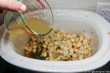 pouring broth into crock pot with vegetables