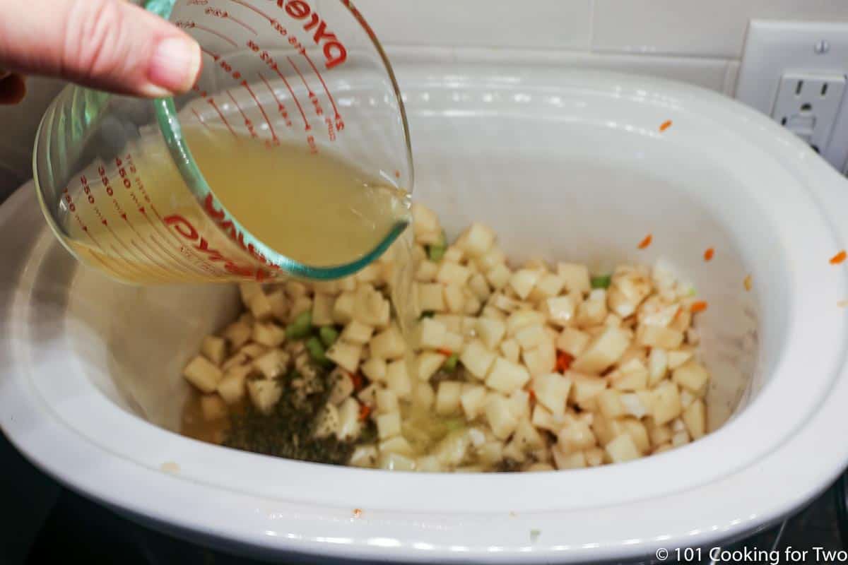 pouring broth into crock pot with vegetables.