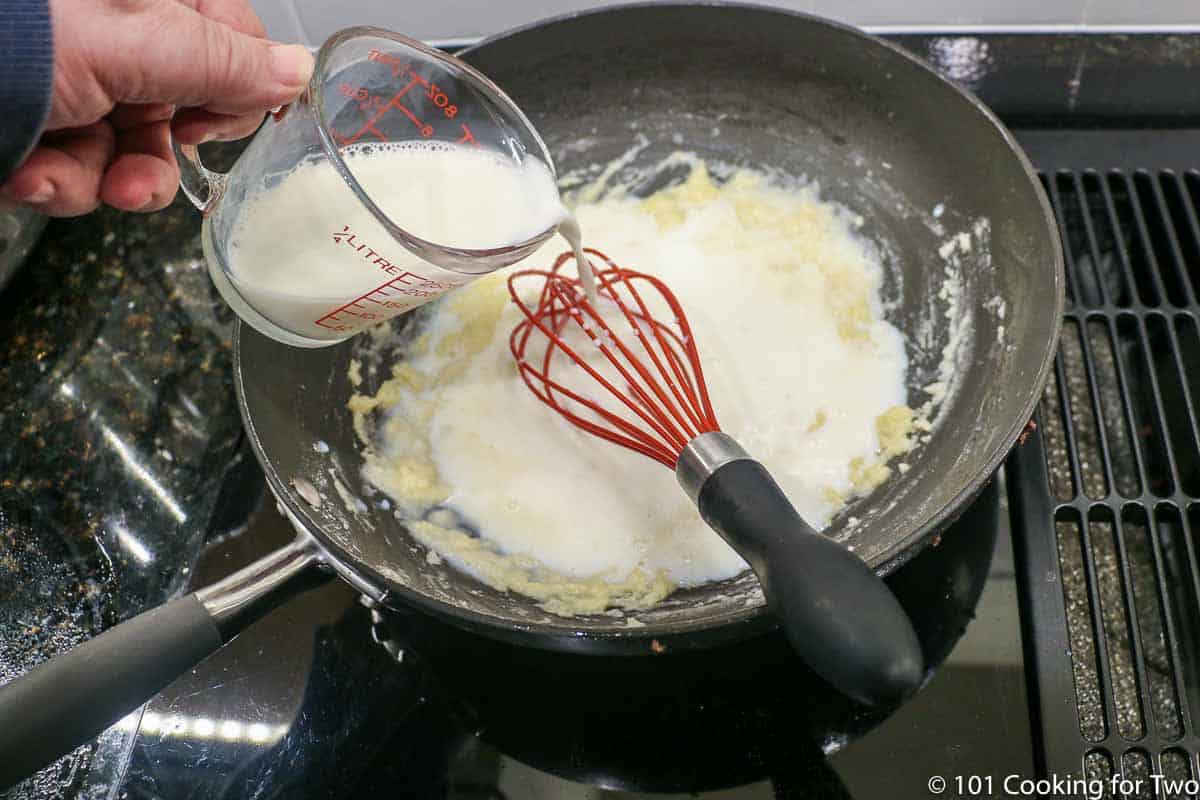 pouring milk into the pan with the roux and whisk.