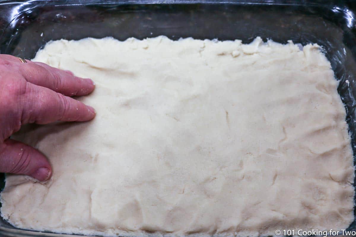 pressing the raw crust dough into the baking dish