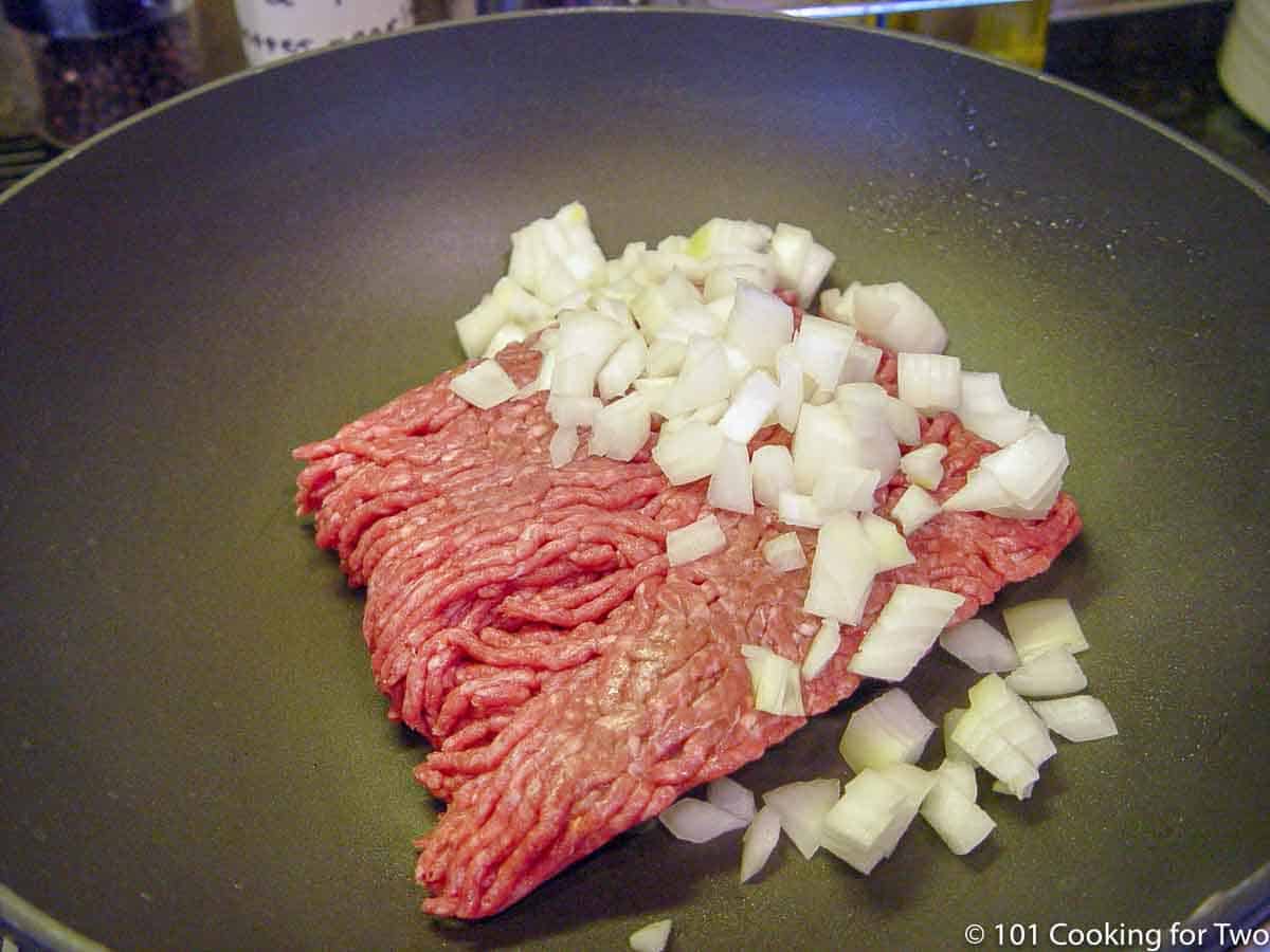 raw burger with chopped onion in frying pan