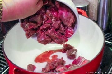 adding chunks of raw beef to dutch oven