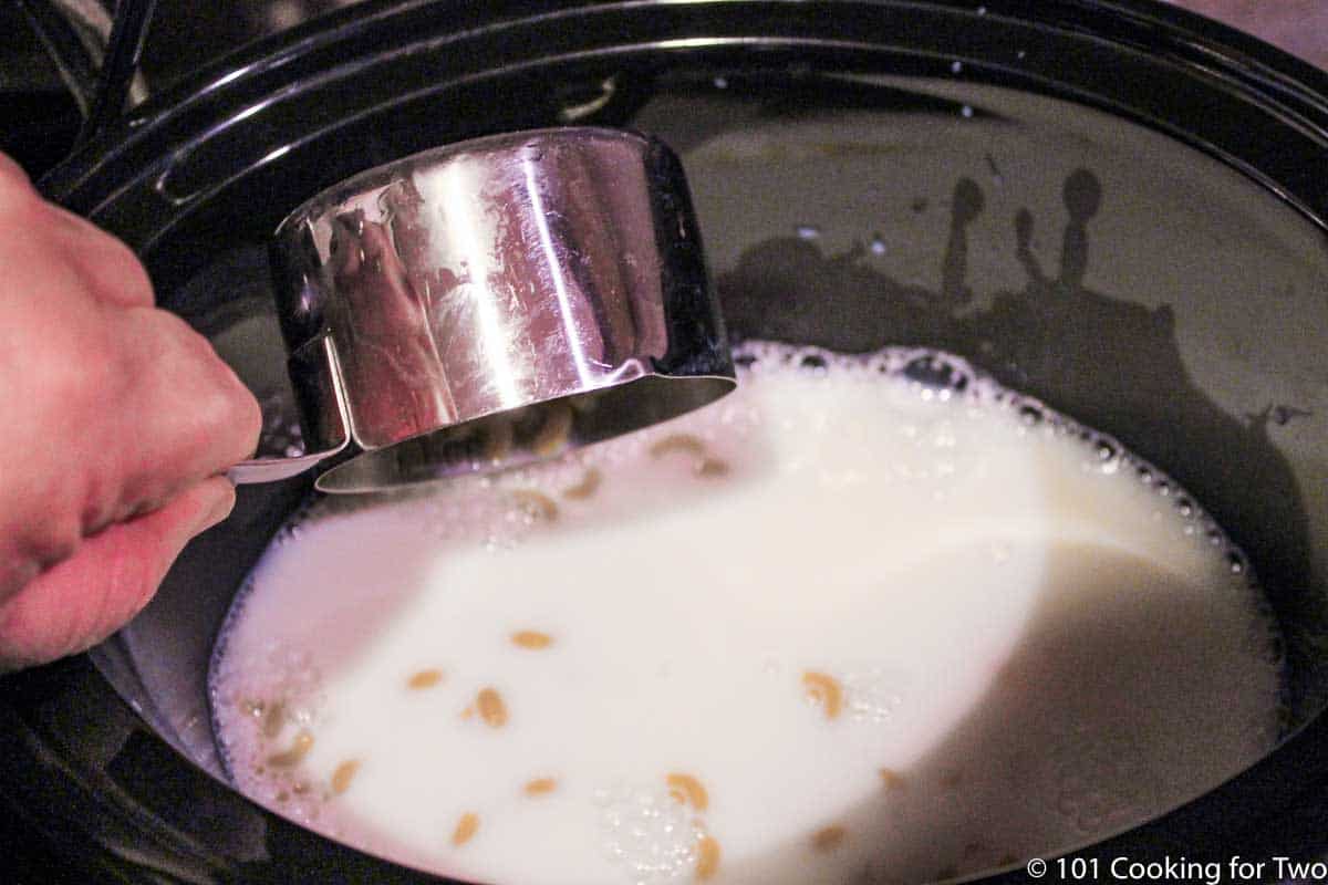 adding dry macarroni to milk in crock pot.