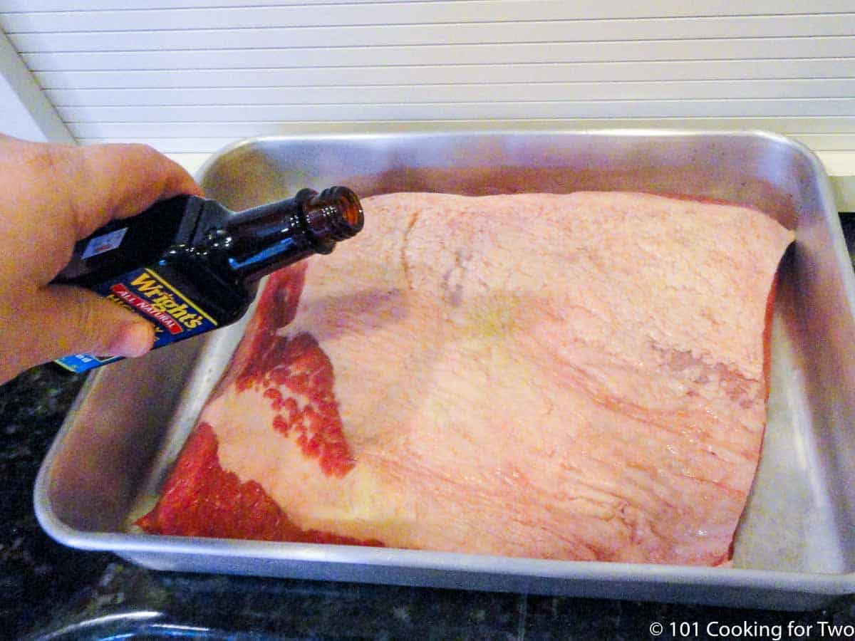 adding liquid smoke to brisket in a cake pan.