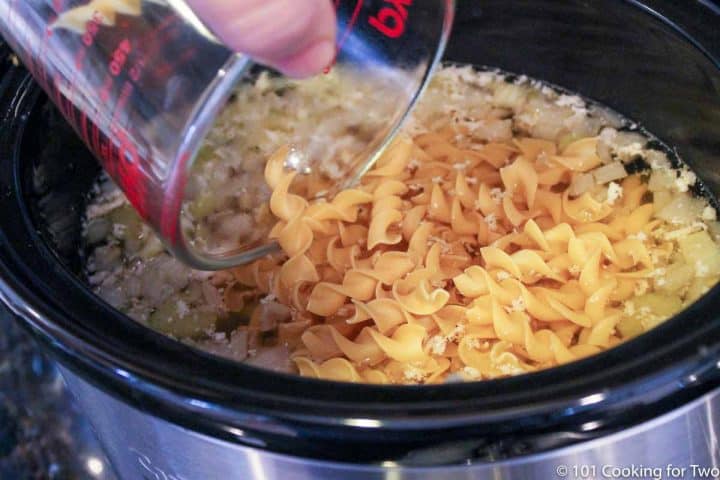 adding pasta to the soup in a crock pot