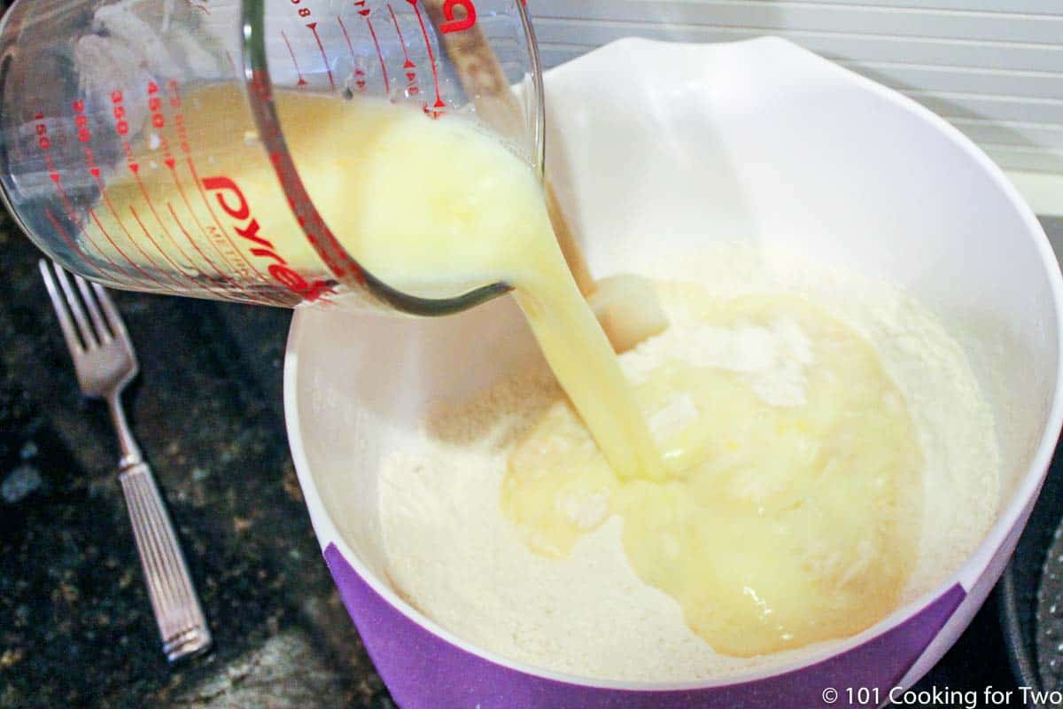 adding wet ingredients into dry in a white bowl.