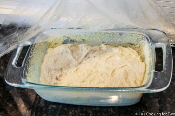 covering the loaf pan and dough with plastic wrap