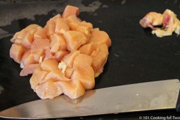 cubes of raw chicken trimmed on a black board