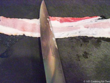 flattening bacon strip on a black board with a knife