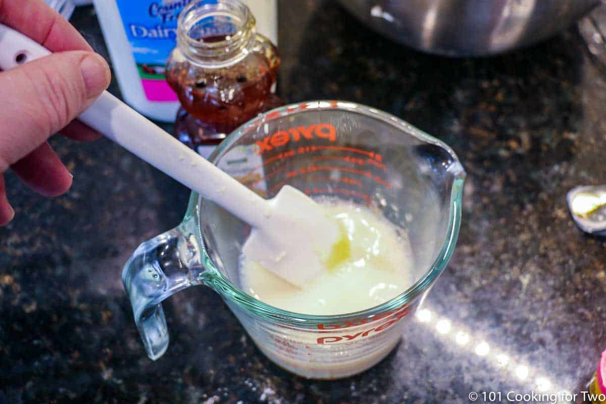 mixing honey into milk in measuring cup.