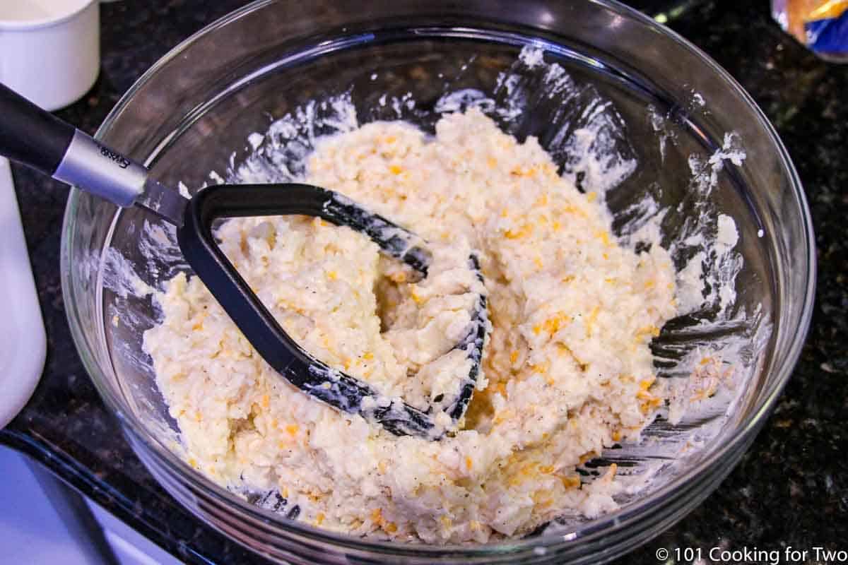 mixing potato with ingredients in a glass bowl.