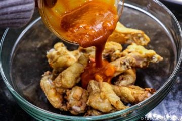 pouring sauce over wings on a glass bowl
