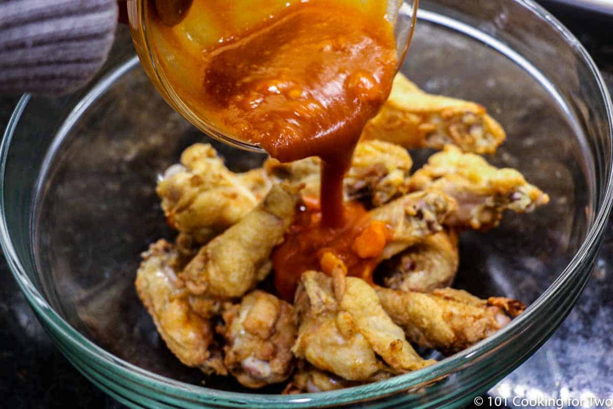 pouring sauce over wings on a glass bowl
