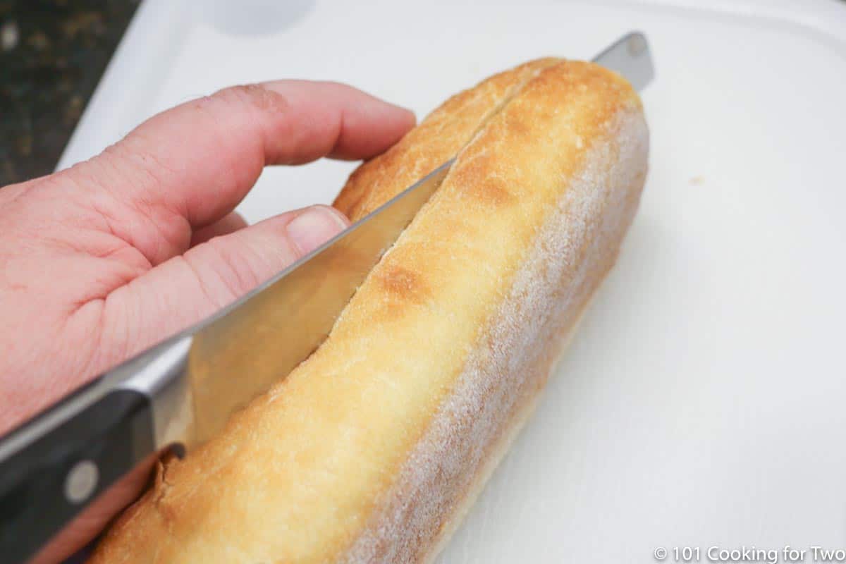 Cutting French bread in half on a white board.