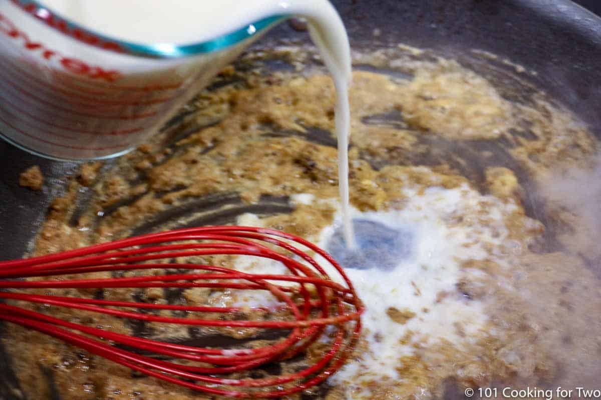 adding milk to the roux in the pan with a whisk.