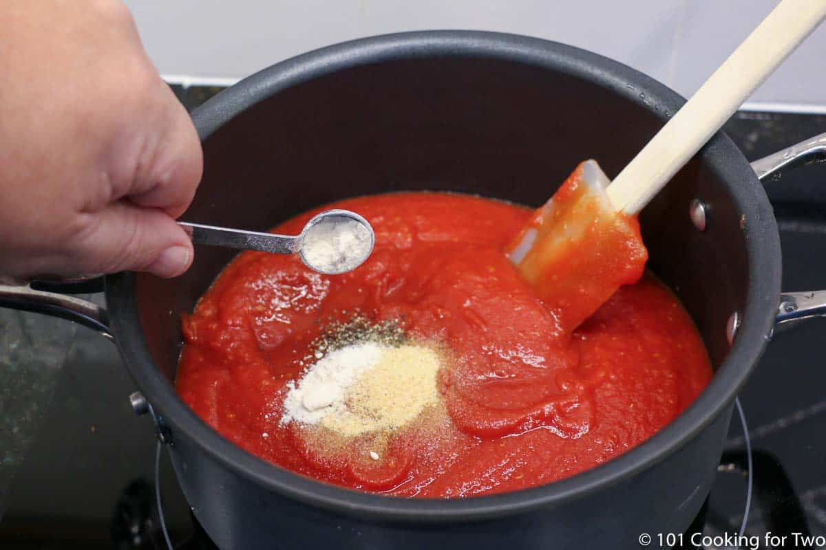 adding spices to tomatoes in a black pan.