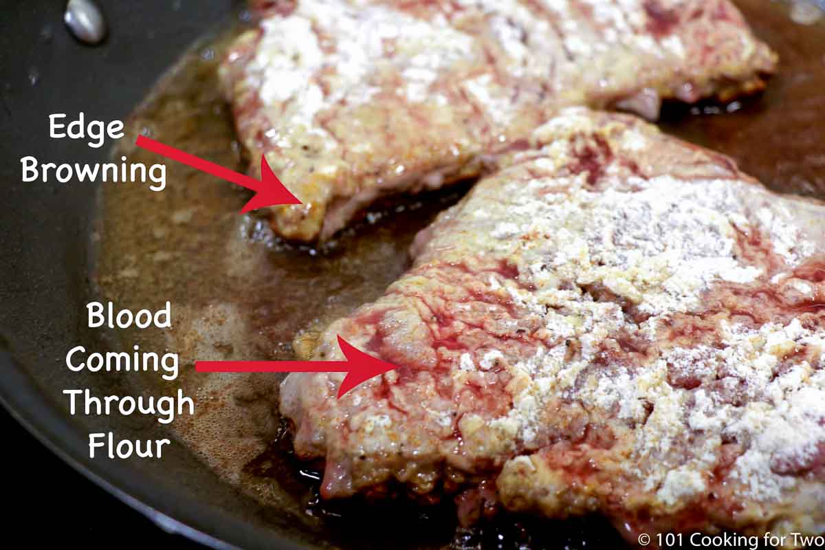 steak in the pan cooking with edge browning and blood starting to come through the flour on top of the steak.