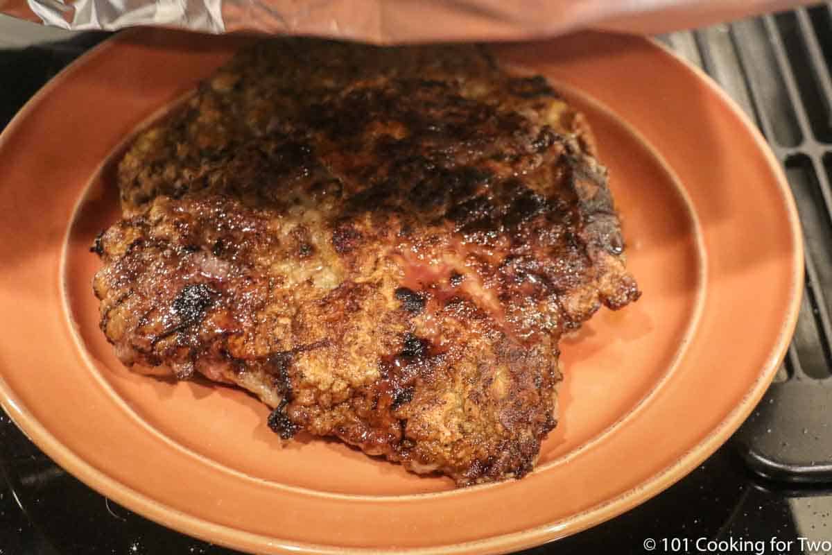 tenting the steak on a plate with foil.