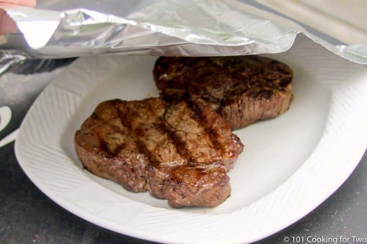 tenting two filets with foil on a white plate