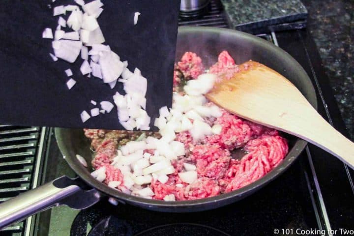 adding chopped onion to burger in a fry pan.