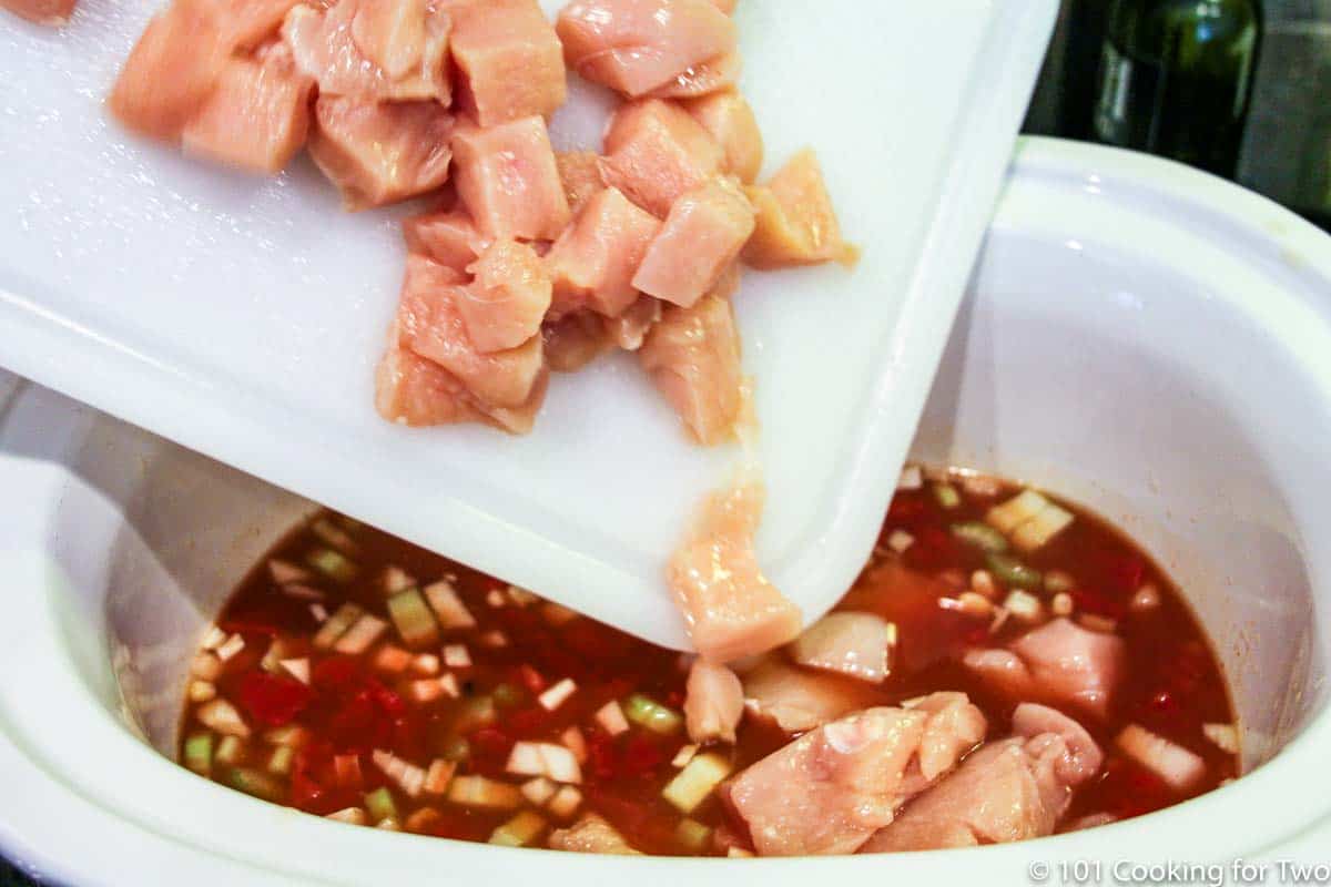 adding cubes of raw chicken to a crock pot.