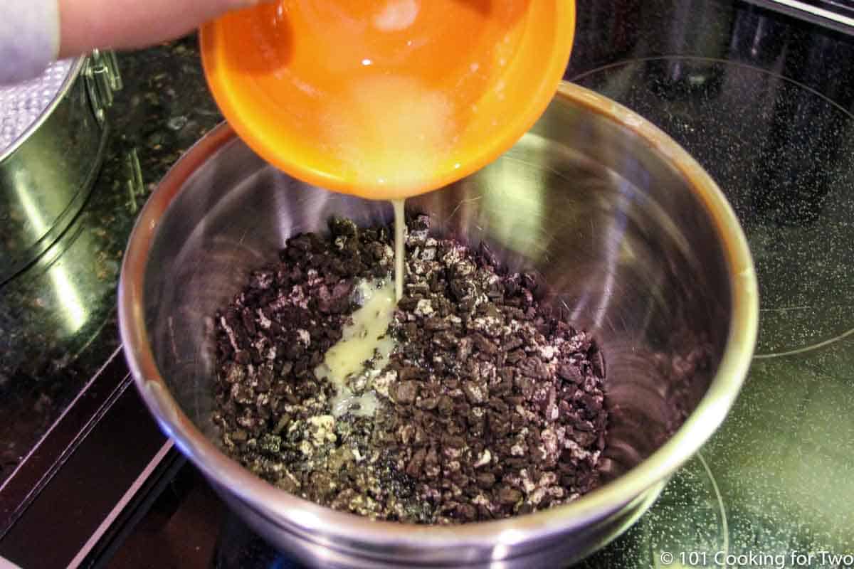 adding melted butter to chopped Oreo cookies