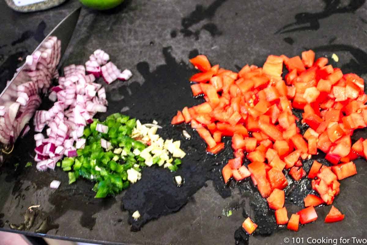 chopped onion with tomato and jalapeno on a black board.