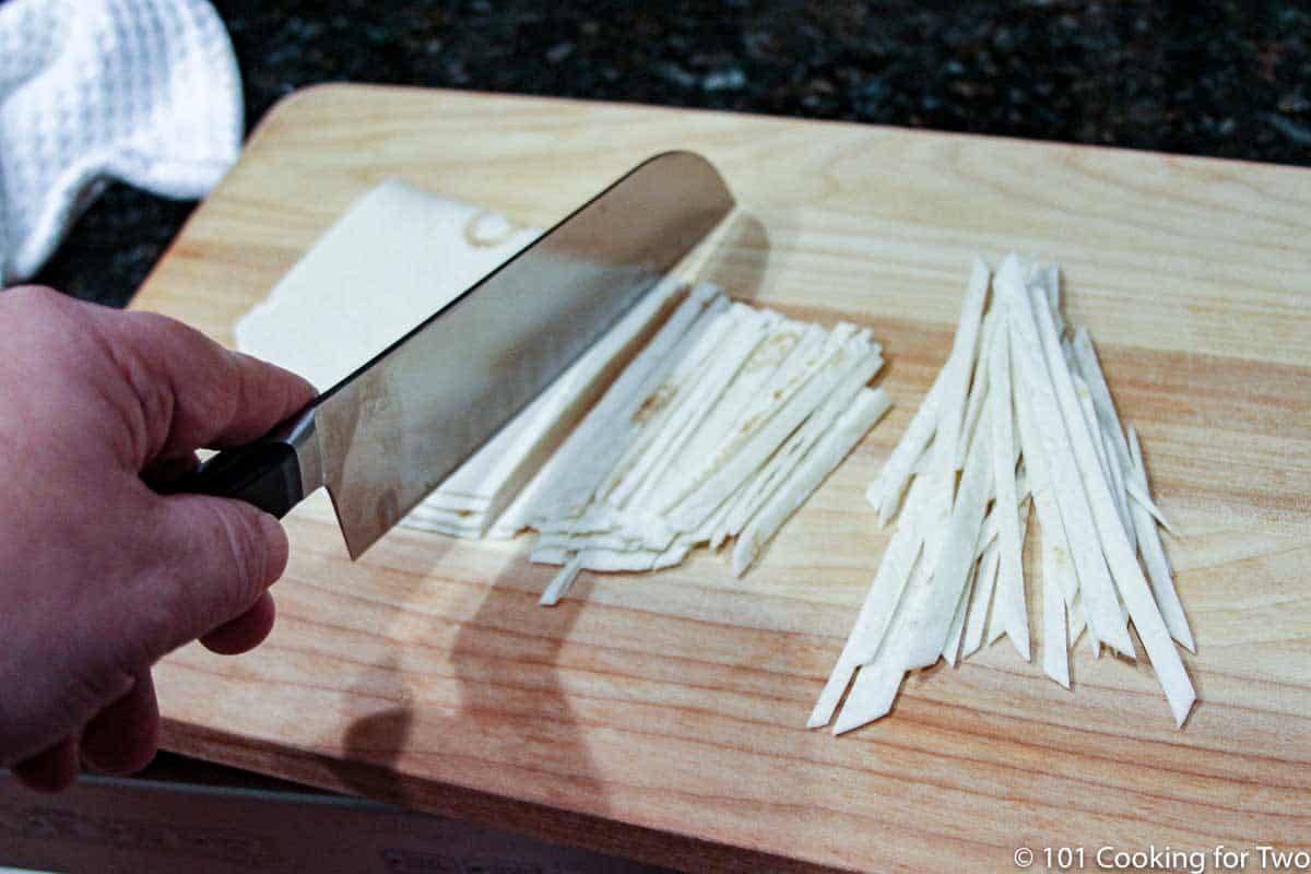 cutting tortillas into stips on a wood board.