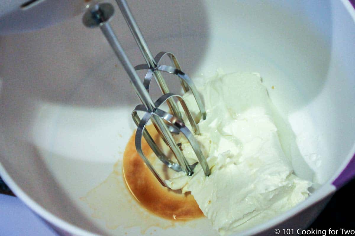 mixing cream cheese frosting in a white bowl with electric mixer.