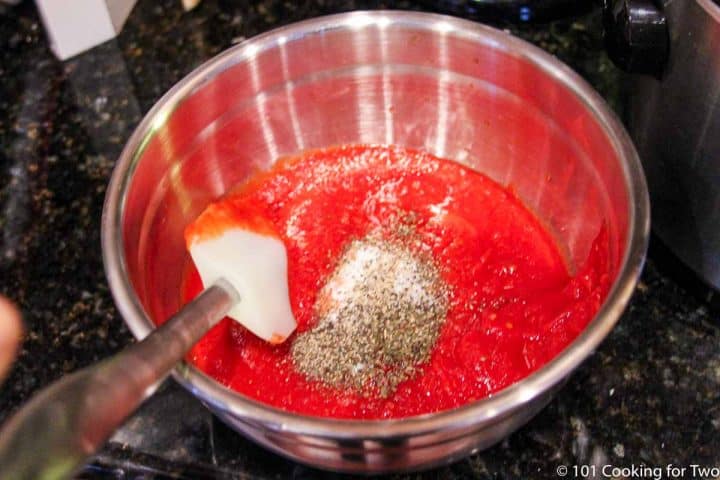 mixing crushed tomatoes with spices in a bowl.