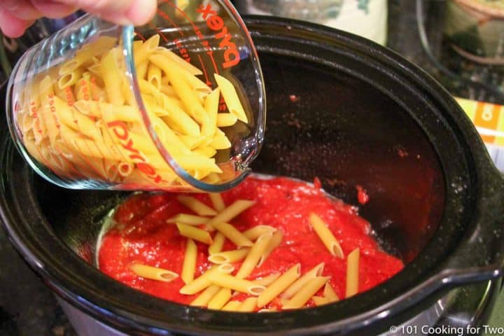 pouring uncooked pasta on the meat sauce.