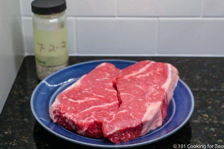 raw strip steaks on a blue plate