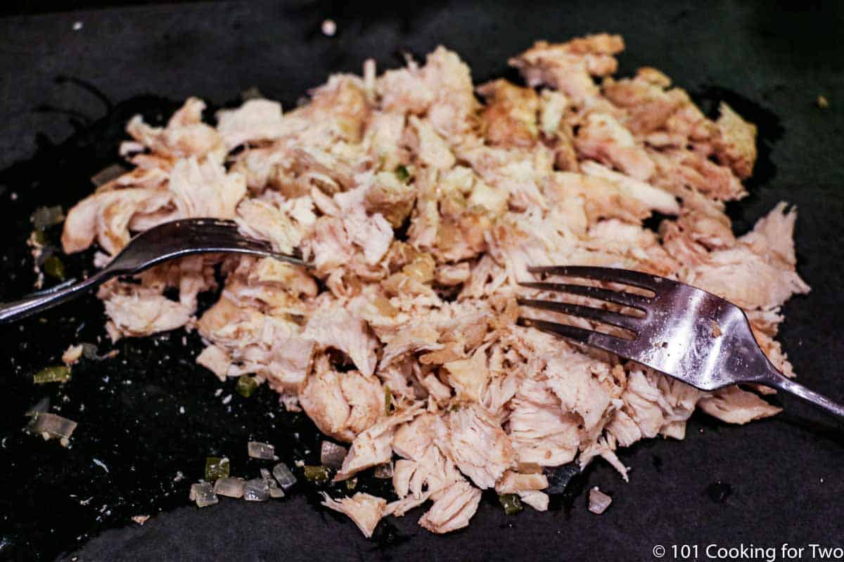 shredding cooked chicken on a black board with forks