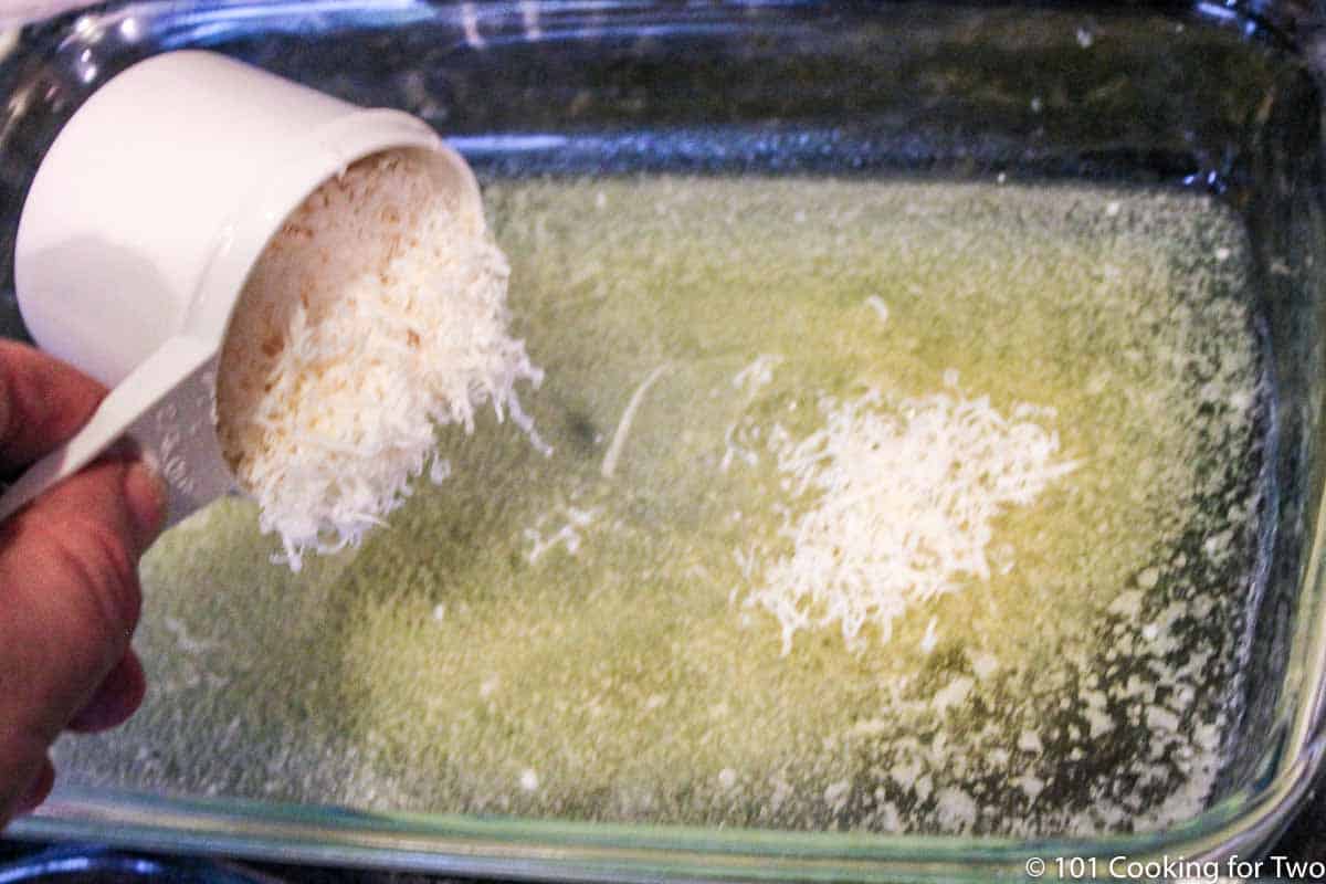 spreading Parmesan cheese over melted butter in a glass bowl.