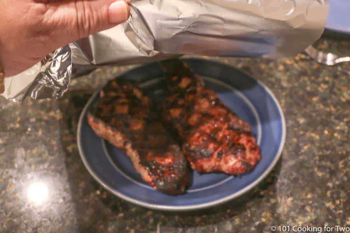 tenting cooked strip steaks with foil.