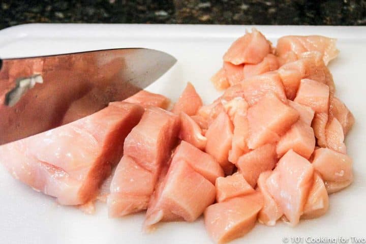 trimmed and cubed chicken on a white board