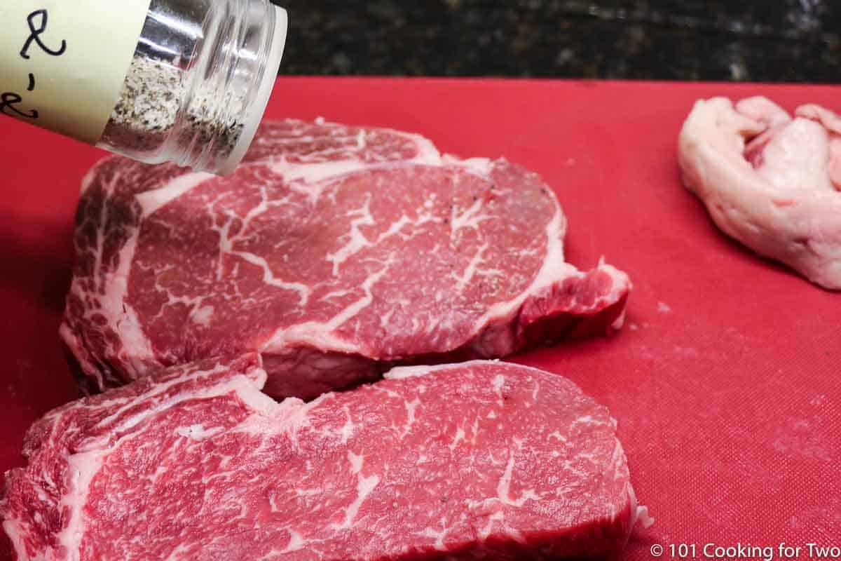 trimmed ribeye steaks being seasoned