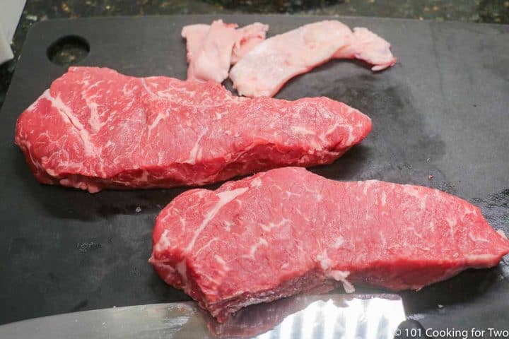 trimmed strip steaks on a black board