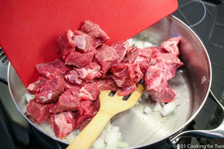 adding cubes of beef to a pan with onion