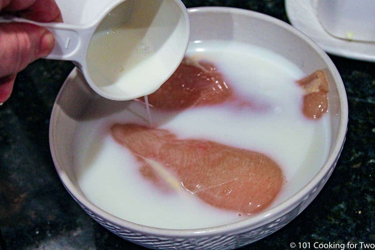 adding milk to raw chicken in a whtie bowl.
