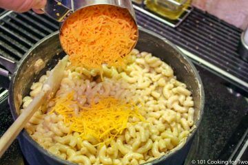 adding shredded cheese to cooked macaroni