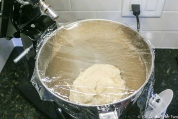 ball of dough in the stand mixer bowl covered with plastic wrap