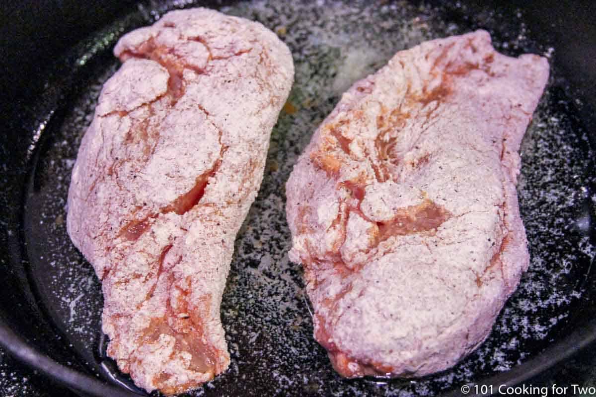 coated chicken breasts in a pan with butter.