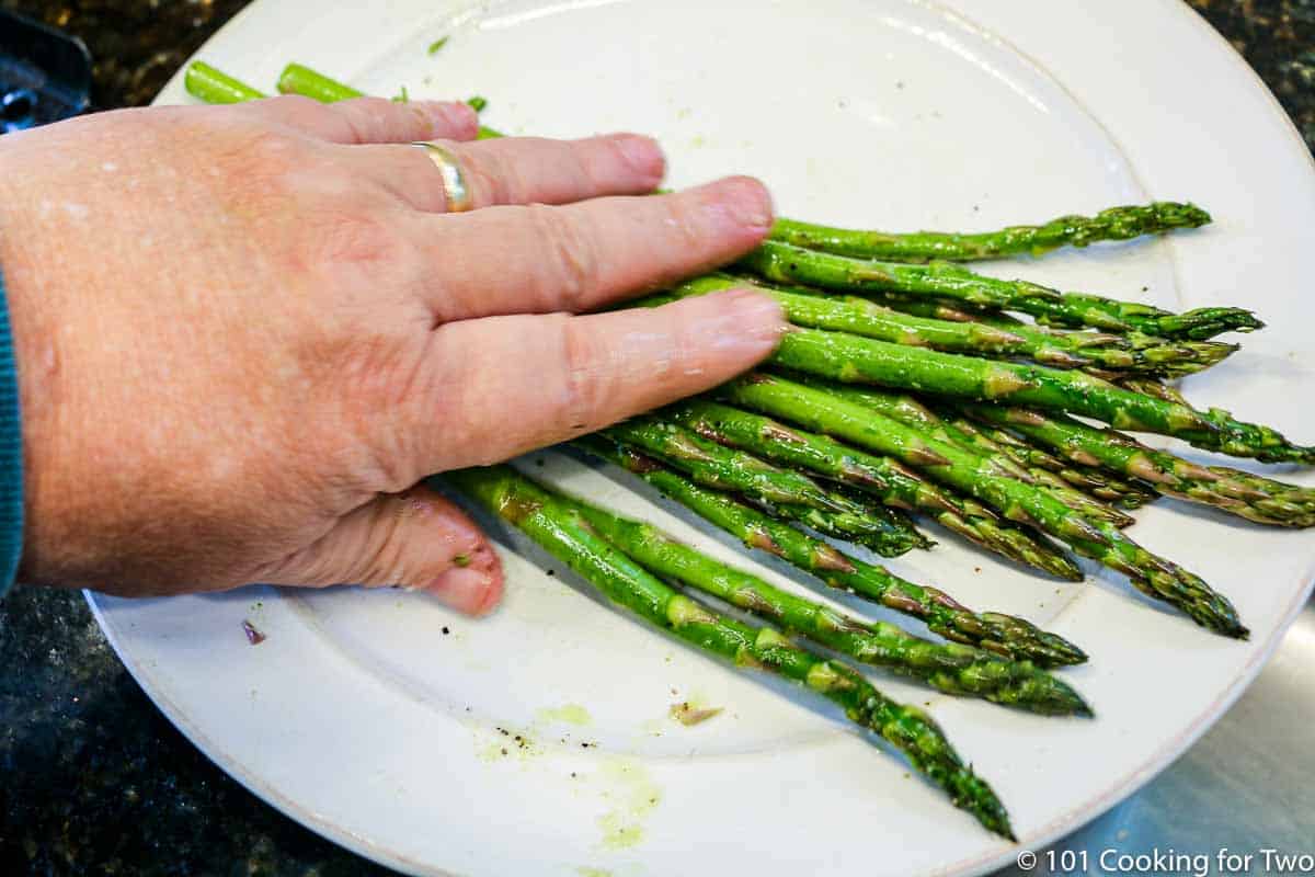 coating asparagus with oil in on plate.