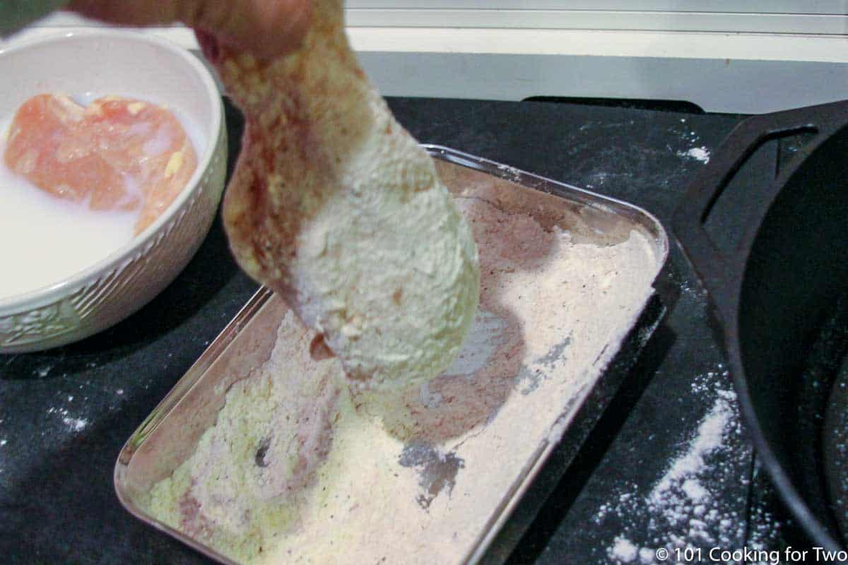 dipping a chicken breast in flour.
