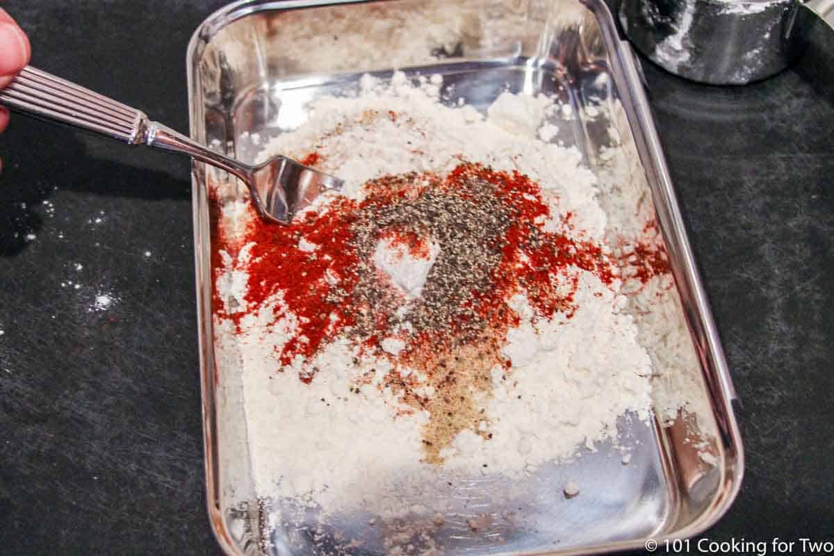 mixing spices with flour in a tray.
