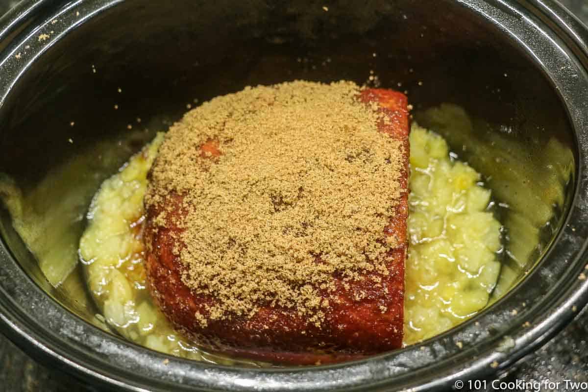 placing the coated ham on the pineapple in the crock pot.