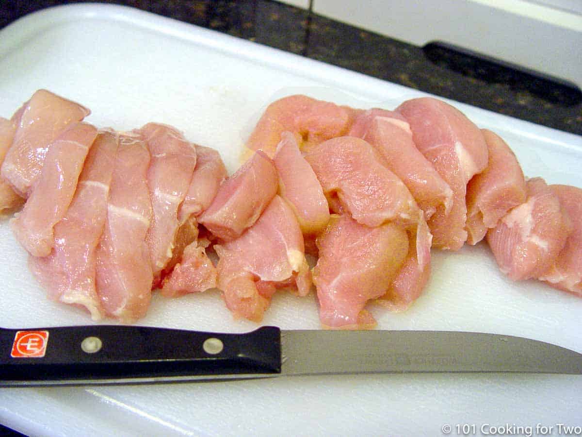 raw chicken breasts sliced on a white board.